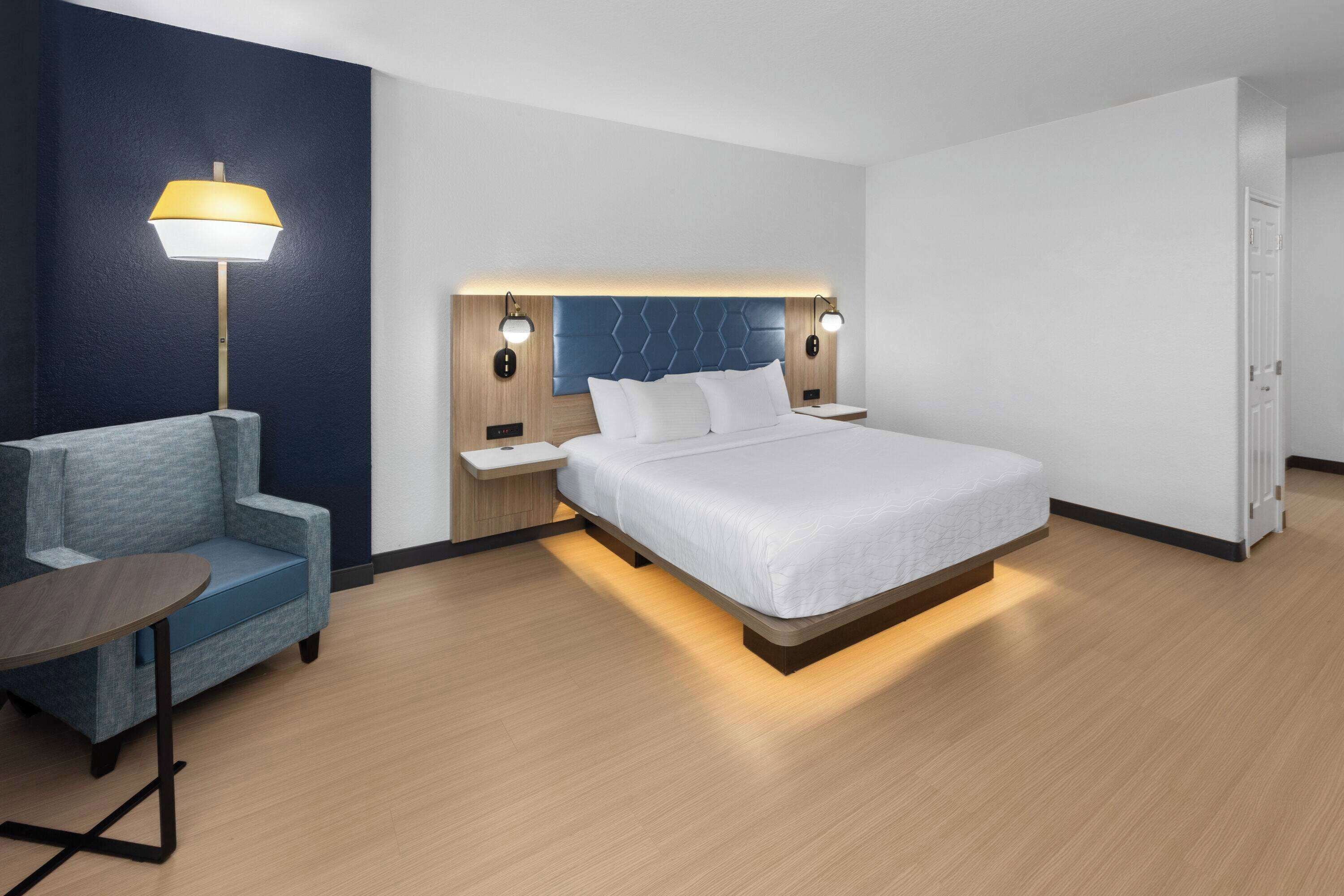 Una habitación de hotel moderna con una cama, una silla, una mesa y una lámpara.