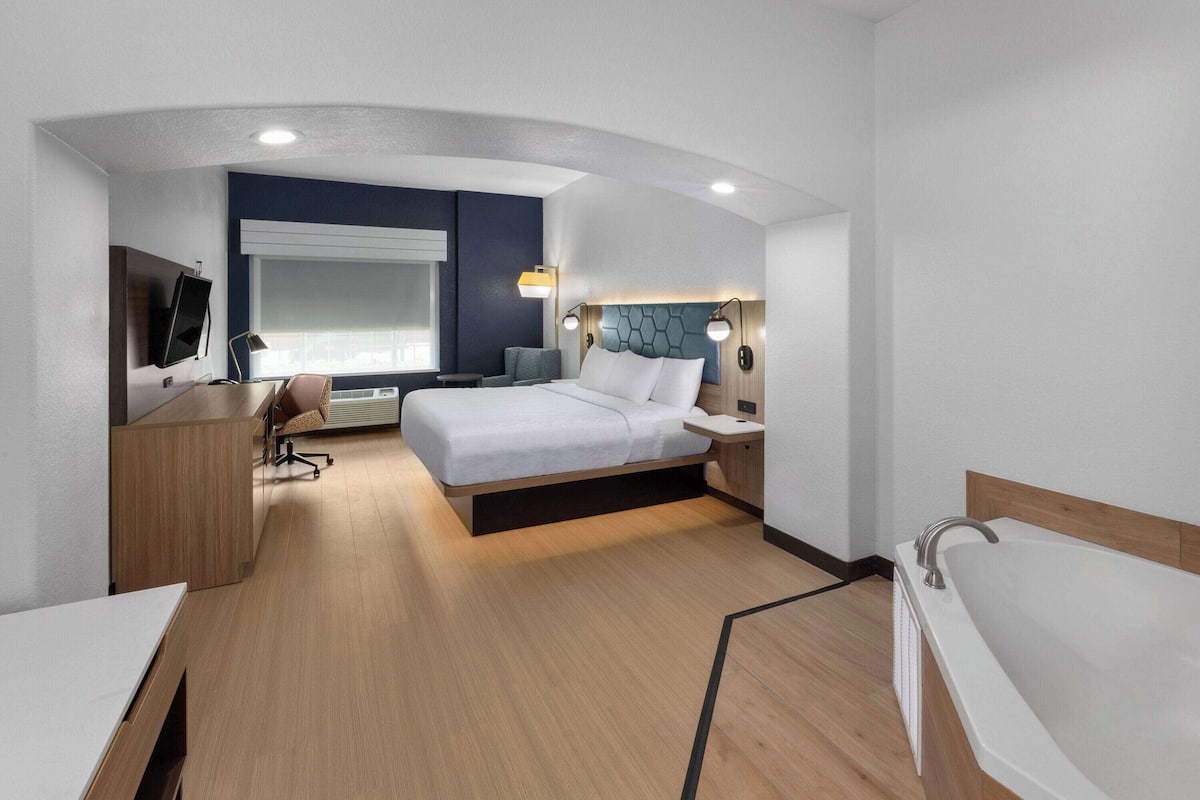 Une chambre d’hôtel moderne, équipée d’un lit, d’un bureau et d’une grande fenêtre.
