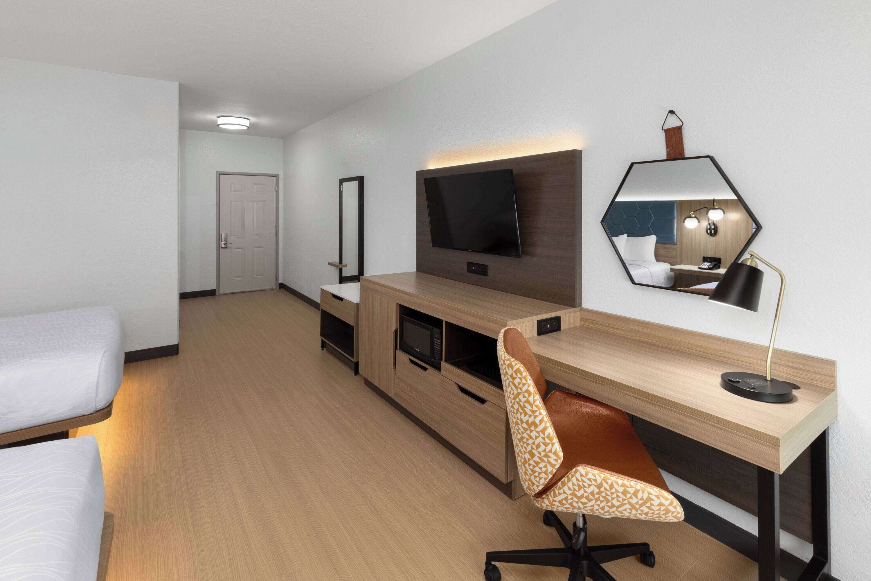 Una habitación de hotel moderna con una cama, un escritorio con una computadora, un televisor y un espejo.