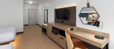 Una habitación de hotel moderna con una cama, un escritorio con una computadora, un televisor y un espejo.