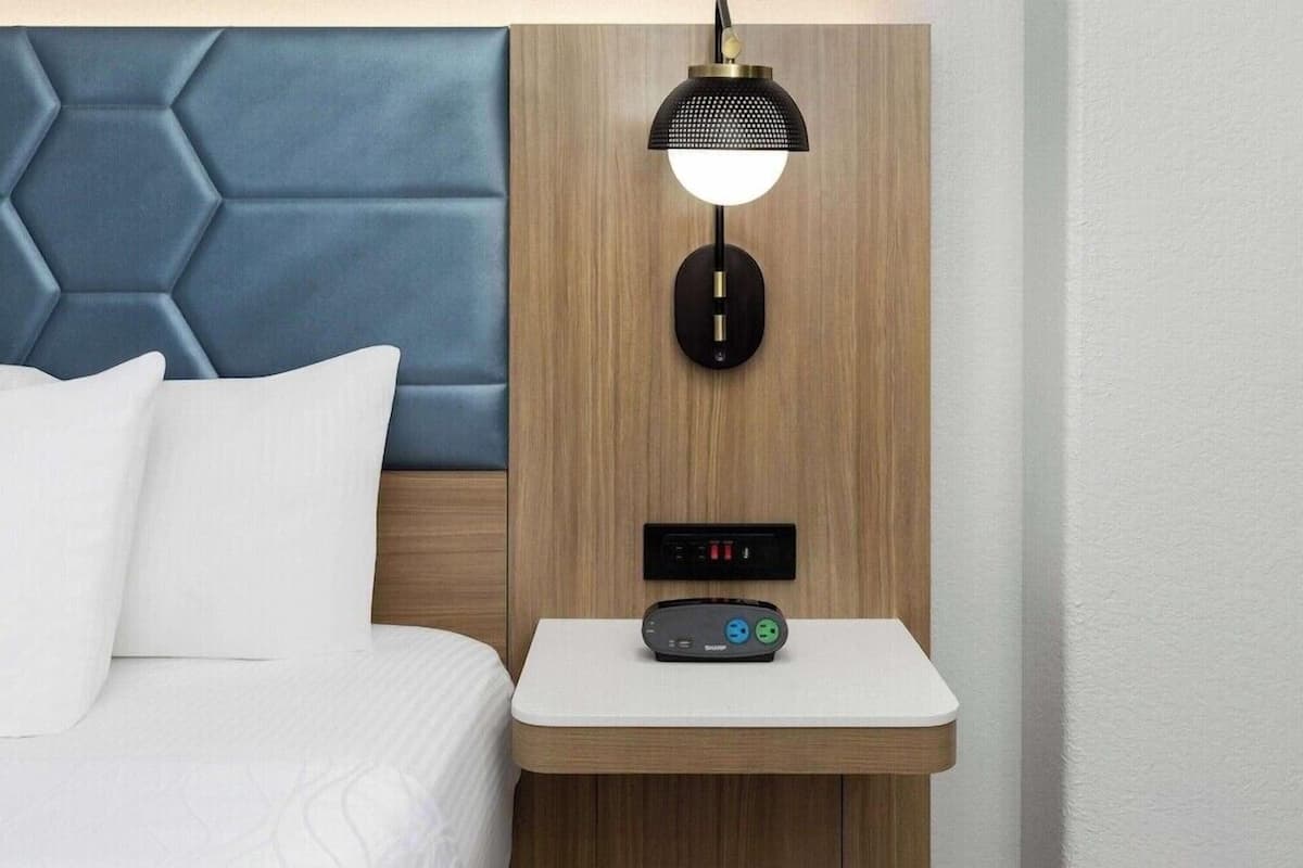 Ein Hotelzimmer mit Bett, Nachttisch mit Lampe und Bedienfeld.