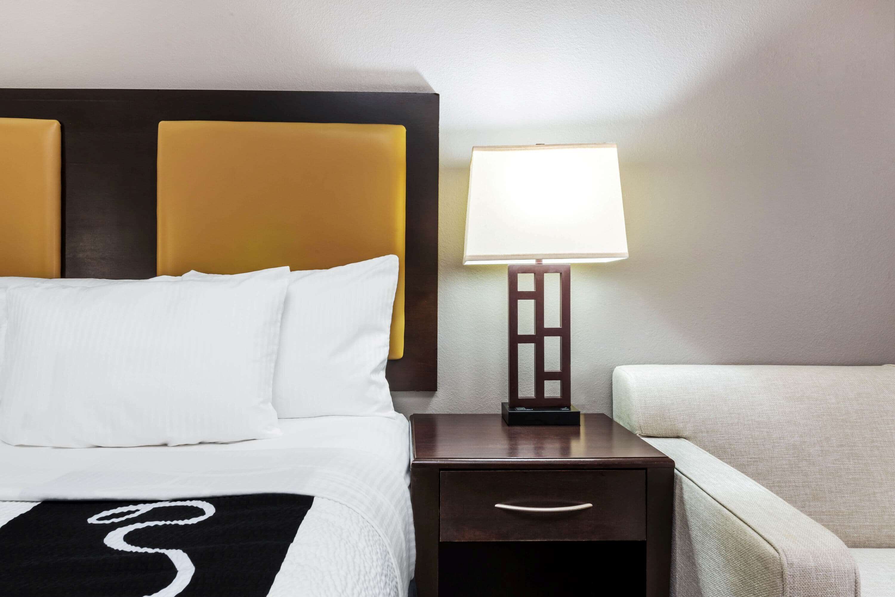 A hotel room with a bed, a nightstand with a lamp, and a sofa.