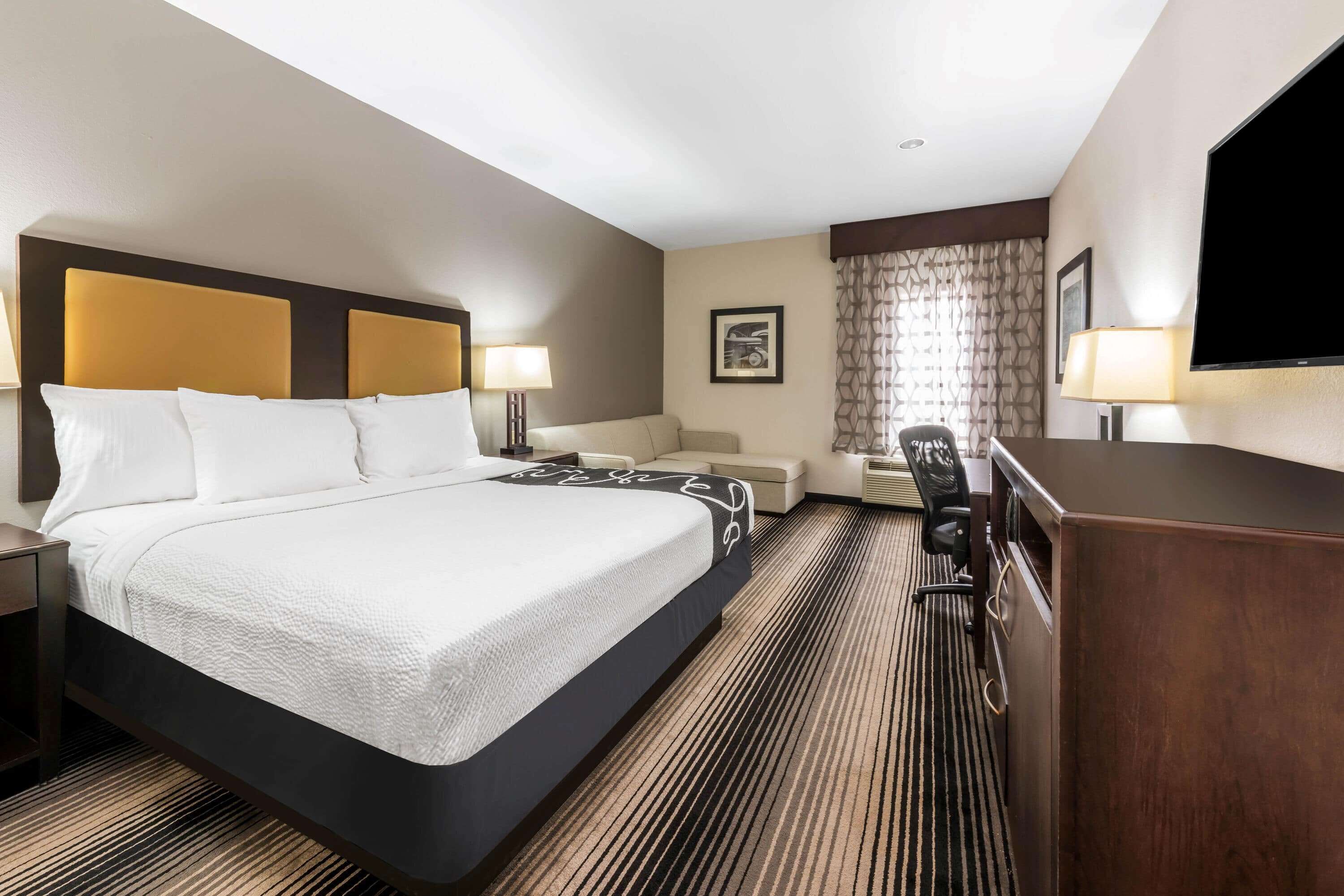 A hotel room with a large bed, a desk, a chair, a TV, and a sofa.