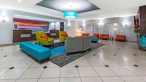 A hotel lobby with a reception desk, colorful seating, a large rug, and a view of the sunset through the window.