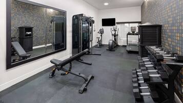 Un gimnasio con equipamiento de ejercicio, una banca y una televisión instalada en la pared.