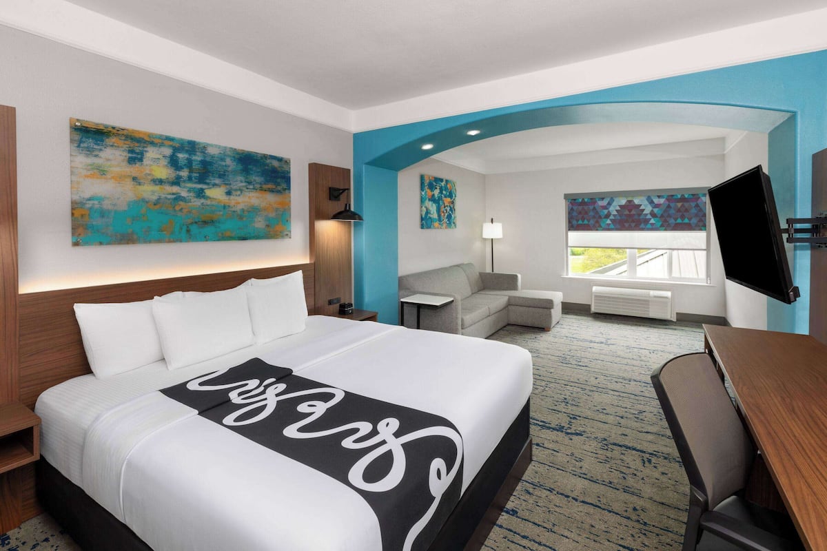 A hotel room with a large bed, a desk, a chair, a TV, and artwork on the walls.