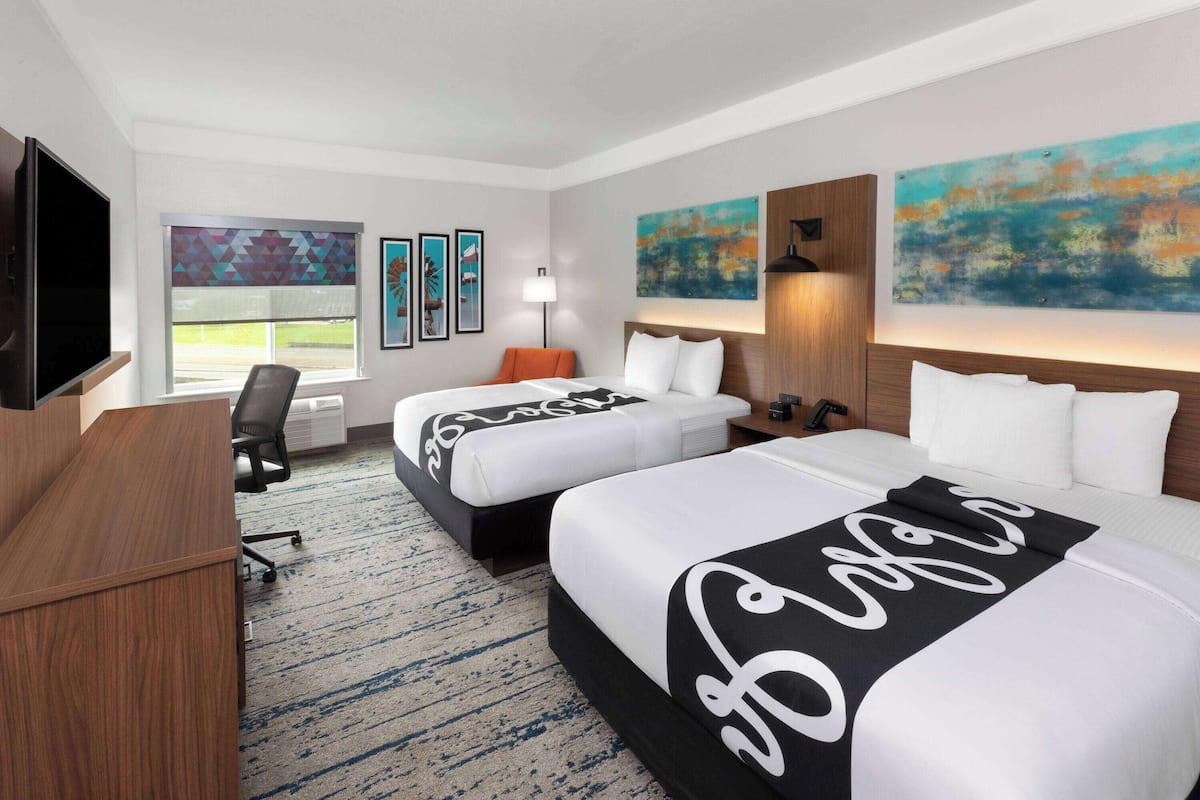 A hotel room with two beds, a desk, a TV, and artwork on the walls.