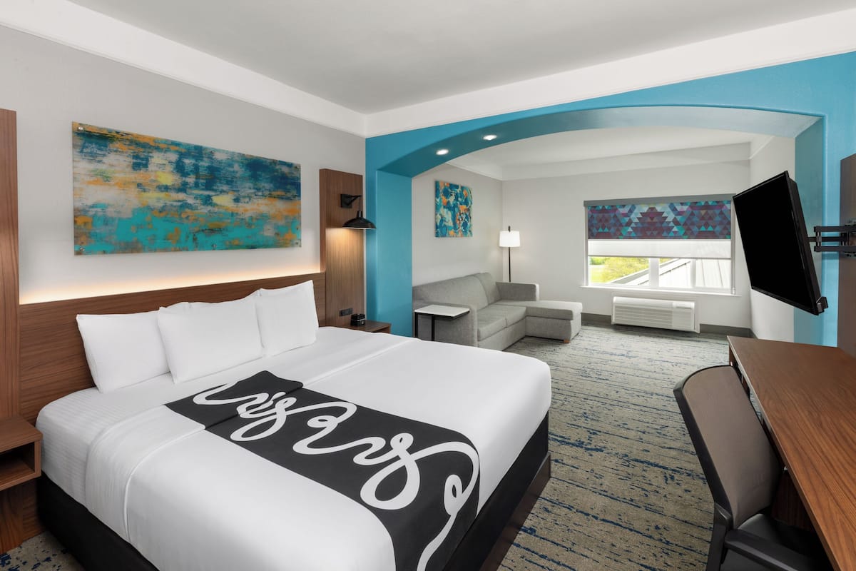 A hotel room with a large bed, a desk, a chair, a TV, and artwork on the walls.