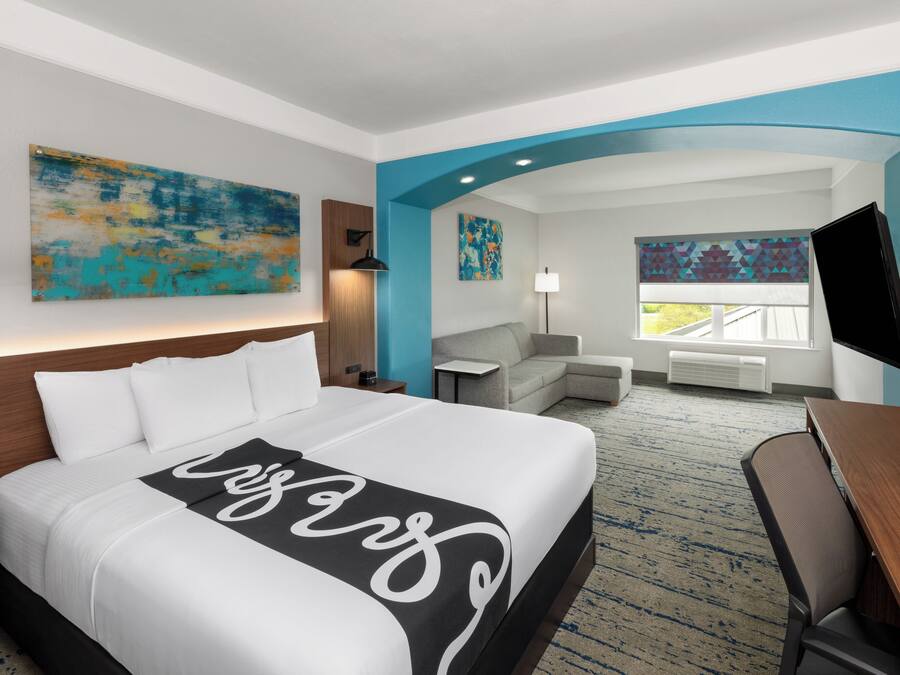 A hotel room with a large bed, a desk, a chair, a TV, and artwork on the walls.