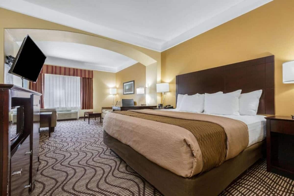 A hotel room with a large bed, a desk, a flat-screen TV, and a window with curtains.