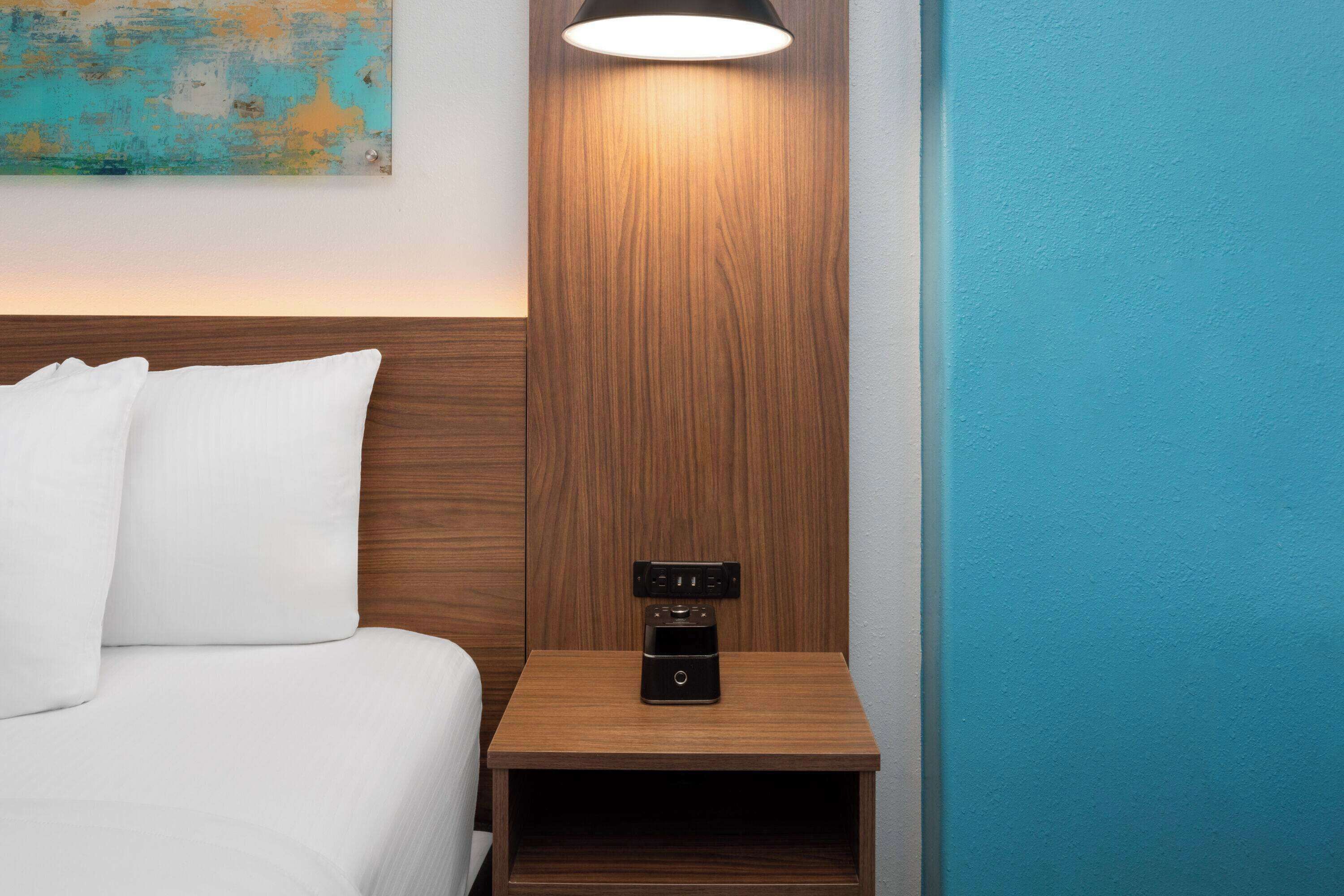 Una cama bien hecha con sábanas blancas, una mesita de noche de madera con una radio negra y una pared color aguamarina.