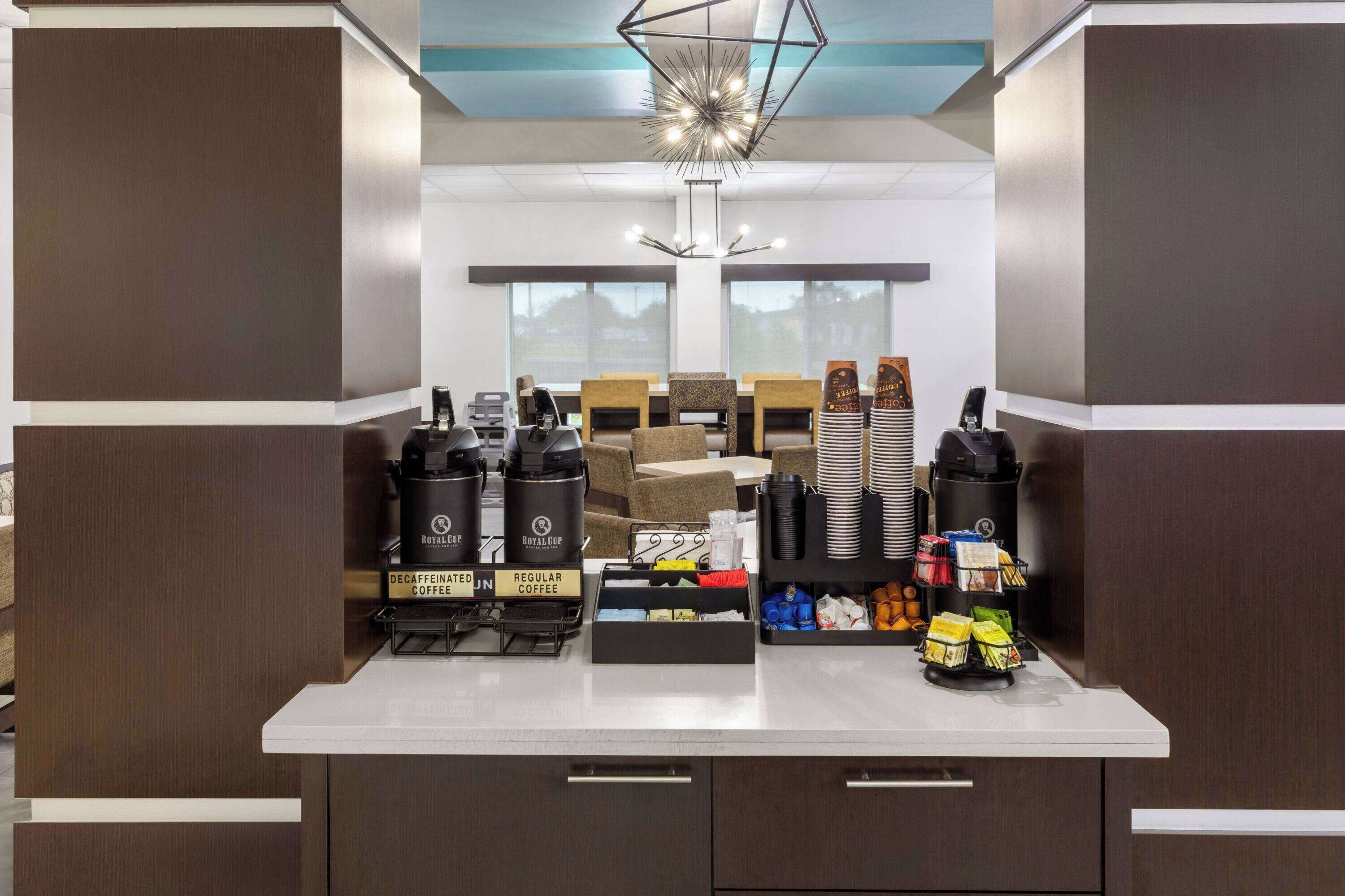 A modern kitchen with a coffee station featuring decaffeinated and regular coffee options, a variety of coffee pods, and a decorative light fixture.