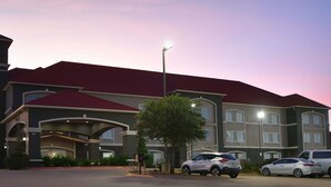 A hotel with a prominent sign, multiple parking spaces, and a well-lit entrance. - La Quinta Inn & Suites by Wyndham Glen Rose (Glen Rose)
