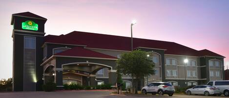 Un hotel con un letrero llamativo, varios espacios de estacionamiento y una entrada bien iluminada.