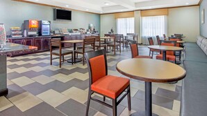 A hotel dining area with multiple tables and chairs, a coffee machine, and a TV mounted on the wall. - La Quinta Inn & Suites by Wyndham Glen Rose (Glen Rose)