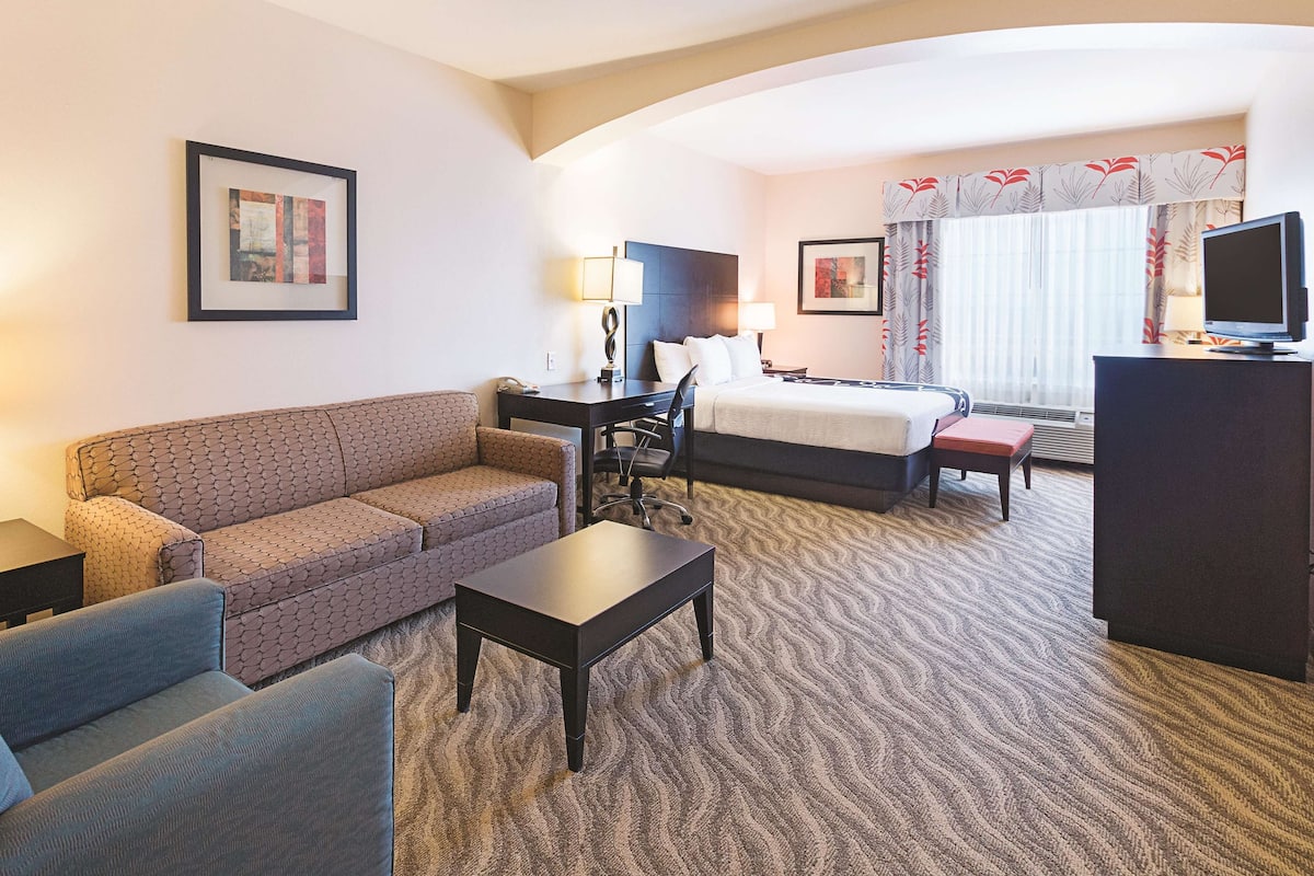 Une chambre d’hôtel équipée d’un canapé, d’un lit, d’un bureau, d’une chaise, d’une télévision et d’une fenêtre avec des rideaux.
