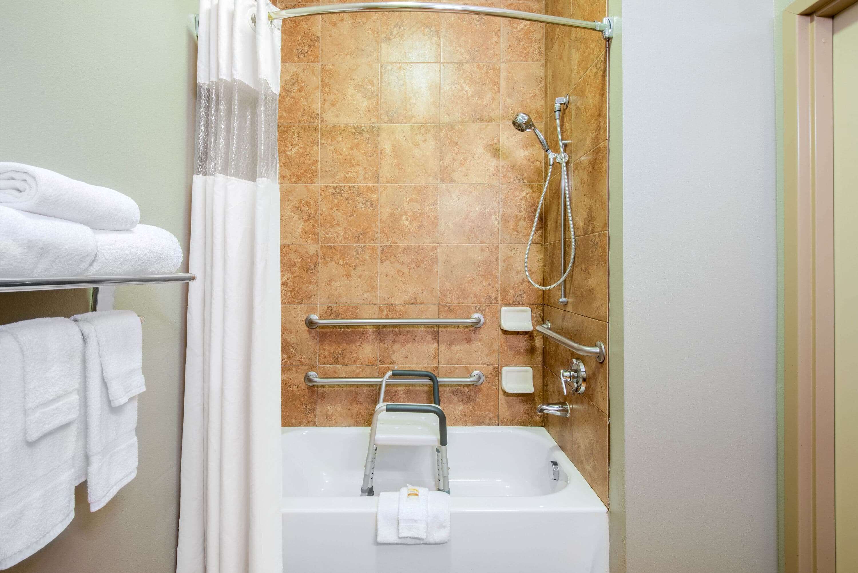 A bathroom with a shower, grab bars, a towel rack, and a soap dispenser.