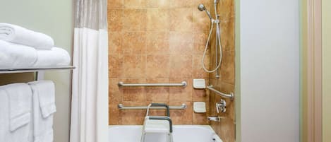 A bathroom with a shower, grab bars, a towel rack, and a soap dispenser.