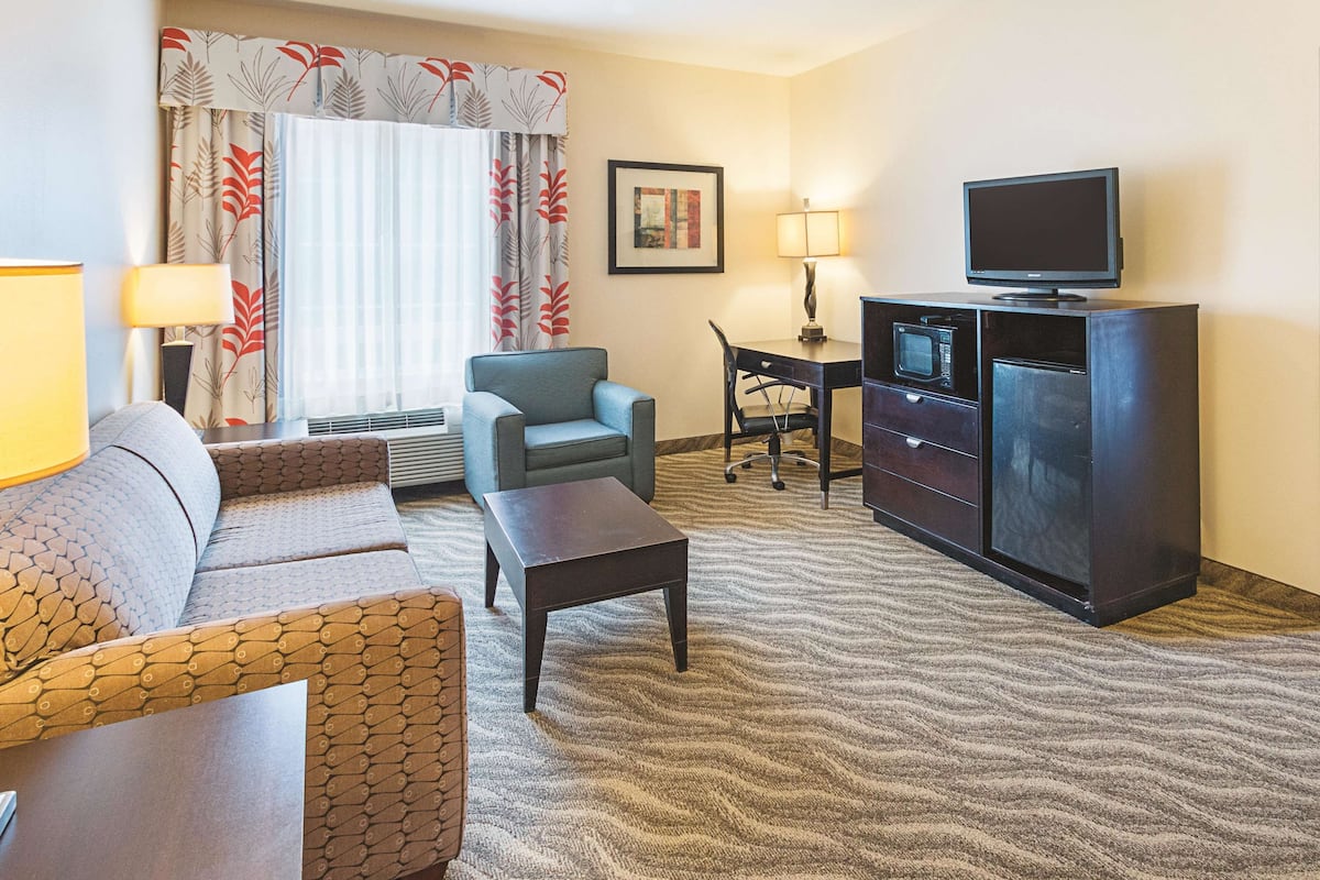 Une chambre d’hôtel équipée d’un canapé, d’un fauteuil, d’un bureau, d’une télévision et d’un mini-bar.