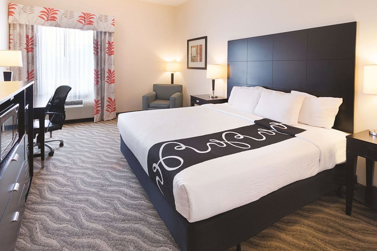 Une chambre d’hôtel avec un grand lit, un bureau avec une chaise, une petite table et une lampe.