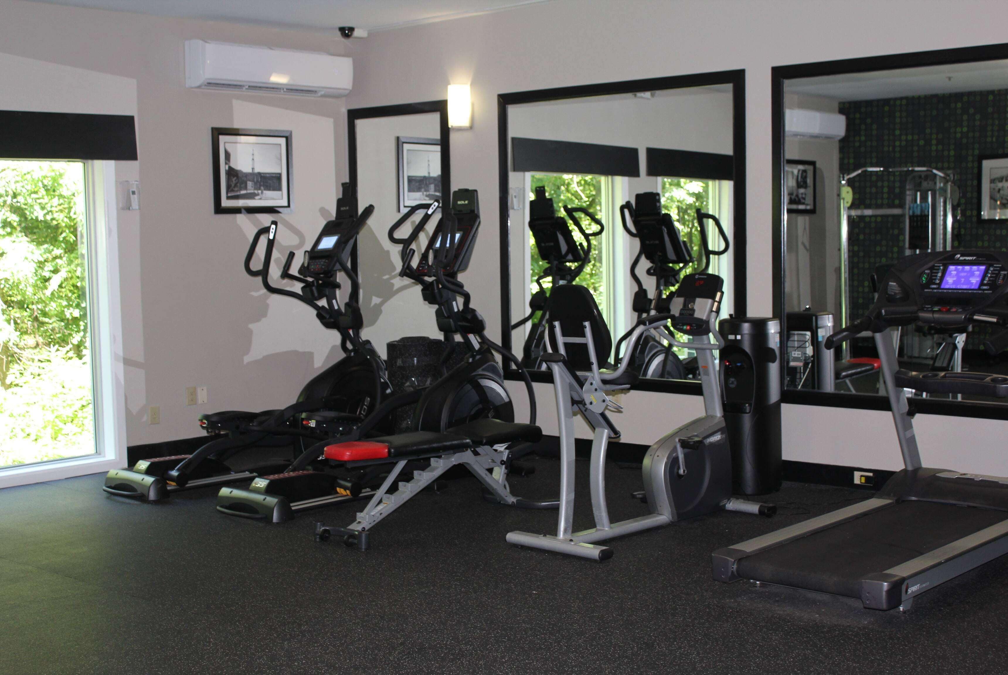 A gym with various exercise machines, a treadmill, and large mirrors on the walls.