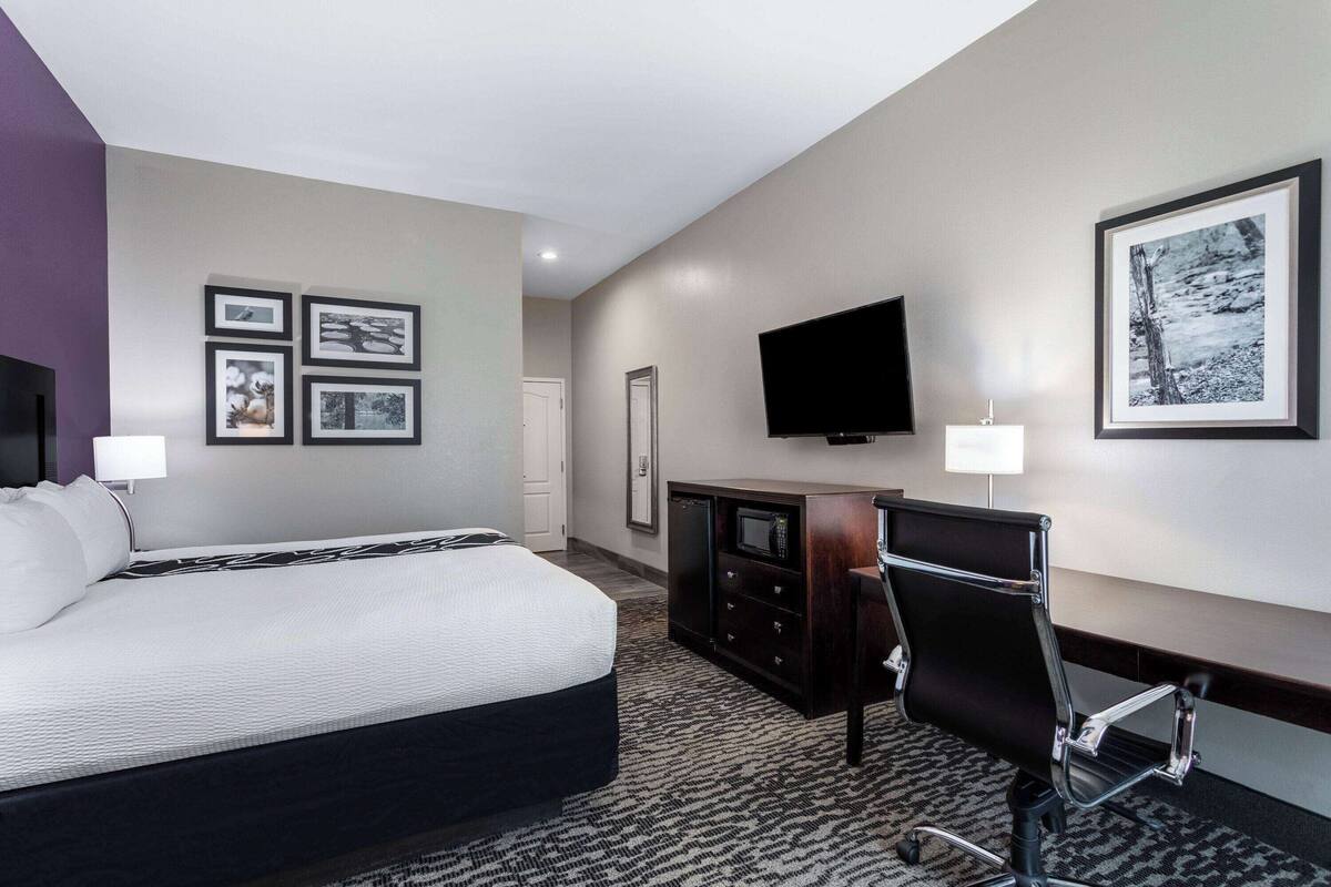 A hotel room with a large bed, a desk with a chair, a flat-screen TV, and framed pictures on the wall.