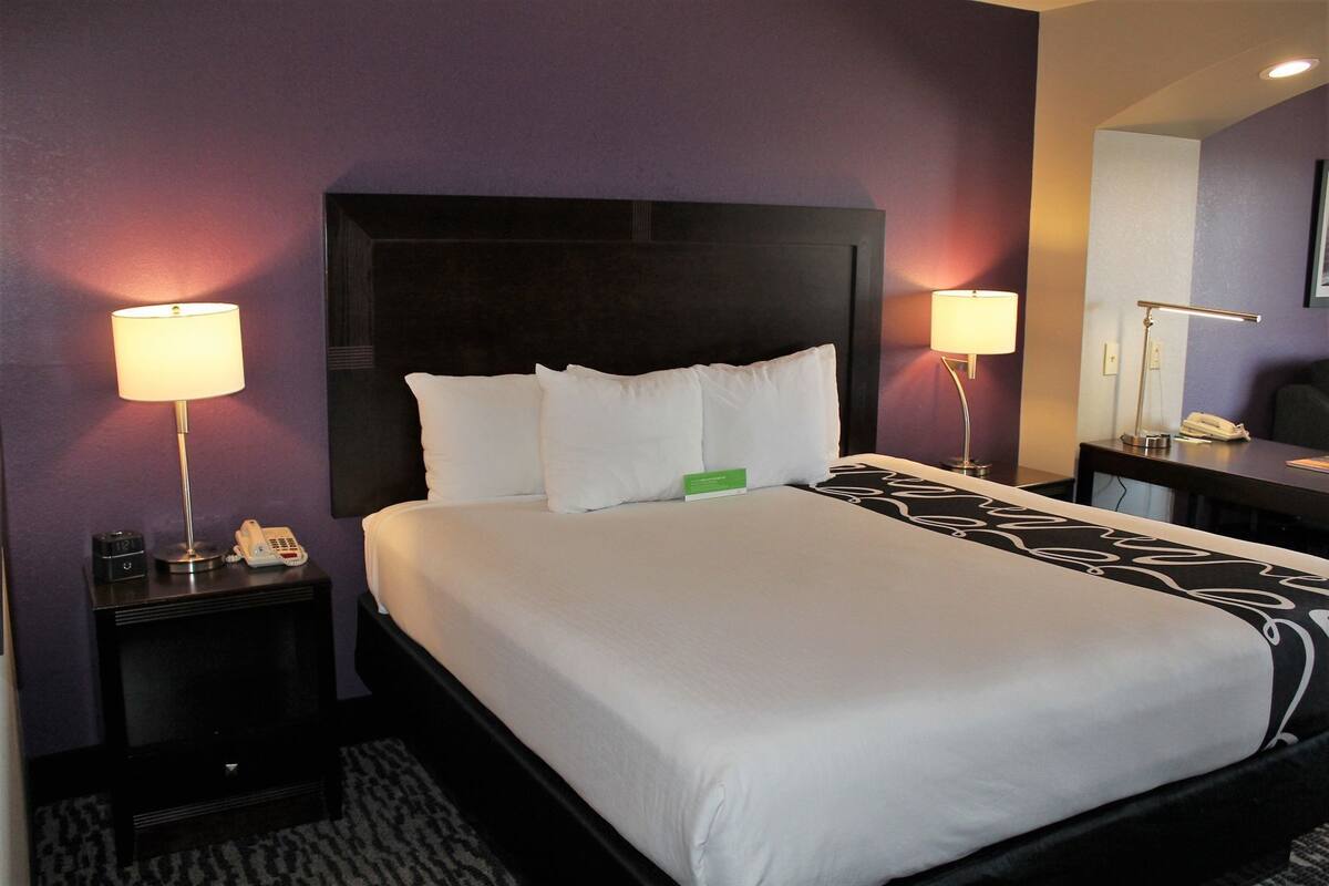 A hotel room with a large bed, two bedside tables with lamps, a desk with a chair, and a mirror on the wall.