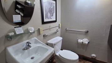 A bathroom with a sink, toilet, and a mirror. There is a framed picture on the wall and a towel rack with towels.