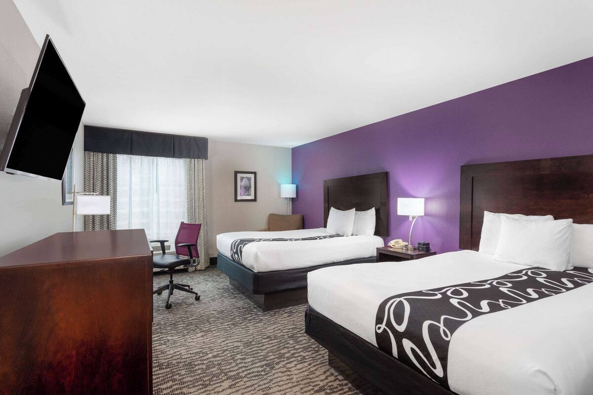 A hotel room with two beds, a desk, a chair, and a TV.