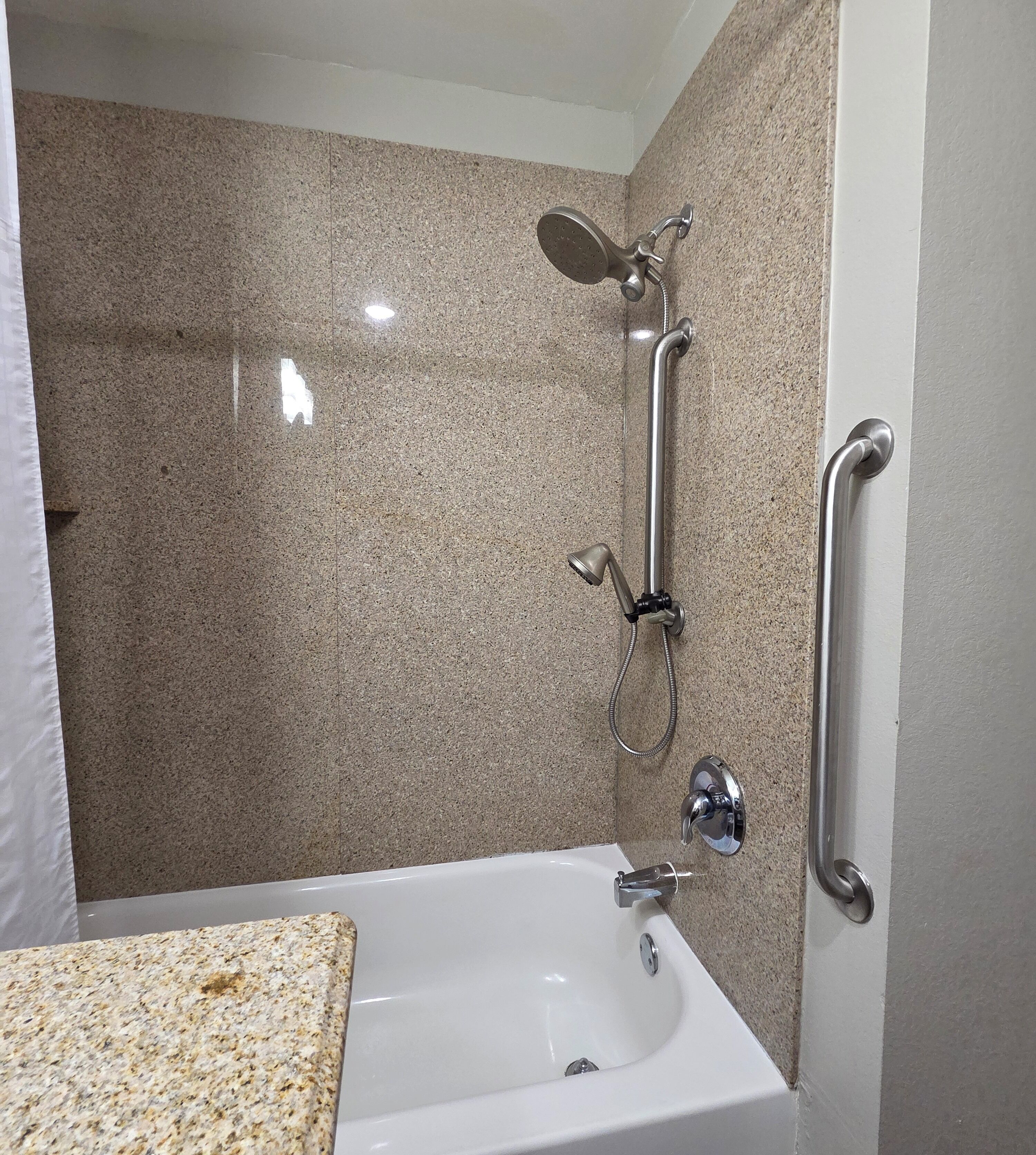Une salle de bain avec un lavabo blanc, une douchette à main et un robinet mural.