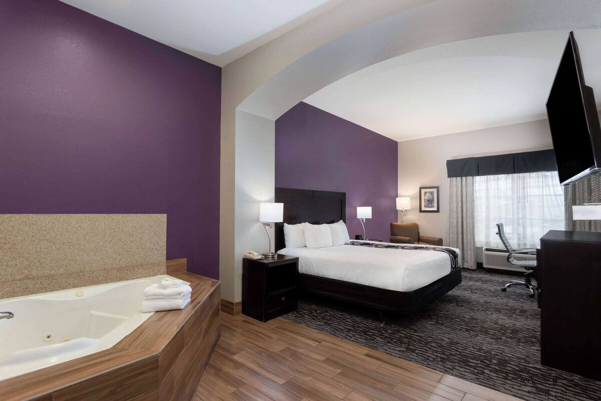 A hotel room with a large bed, a separate bathroom with a bathtub, a desk, and a TV.