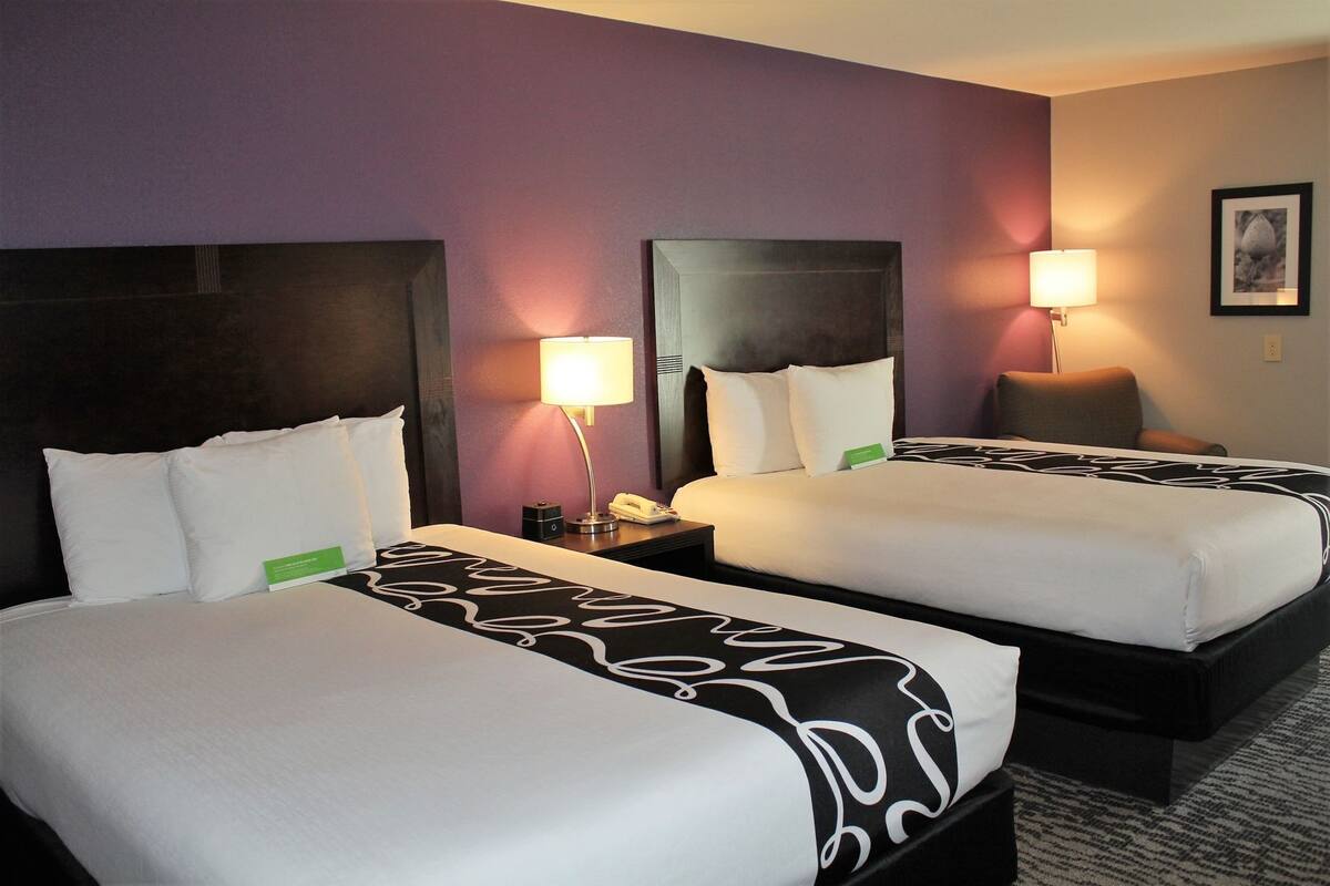 A hotel room with two beds, a nightstand with a lamp, and a framed picture on the wall.