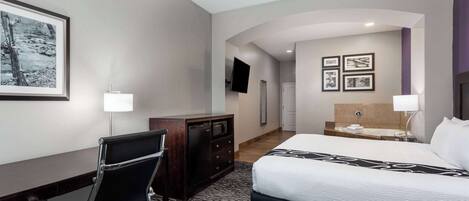 A hotel room with a bed, desk, chair, TV, and artwork on the walls.