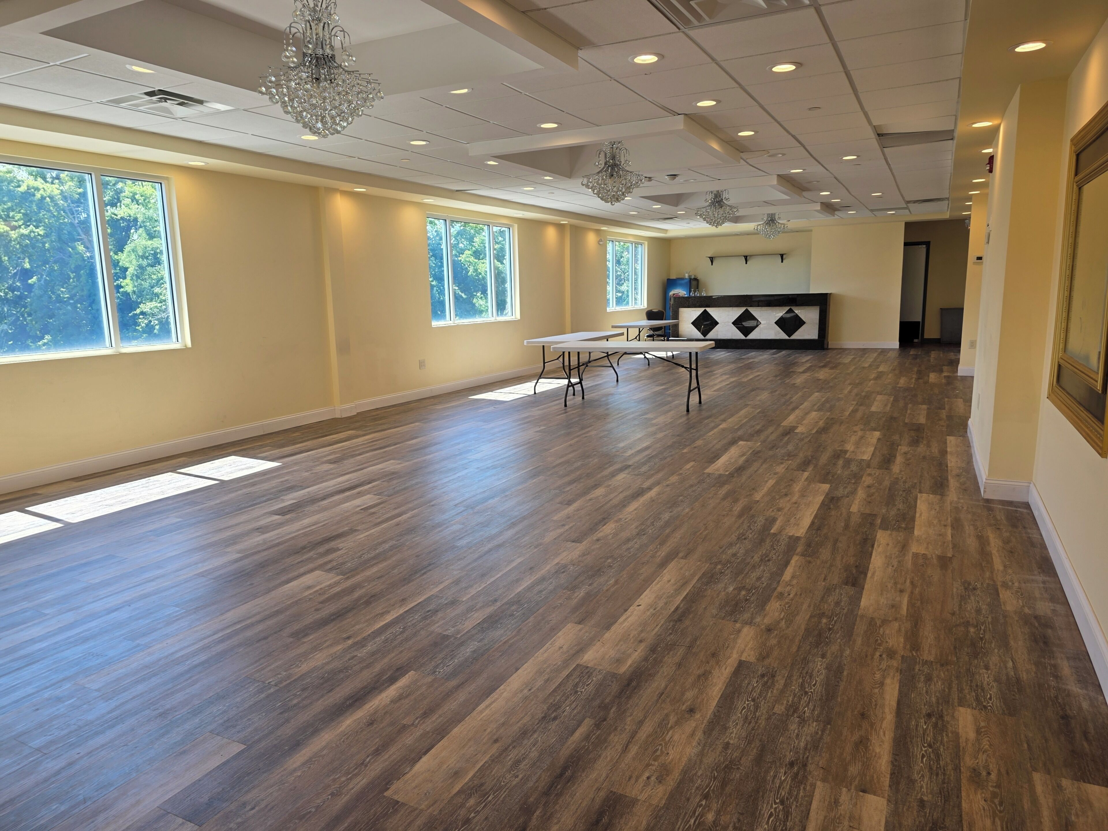 A spacious room with a wooden floor, large windows, and a chandelier.