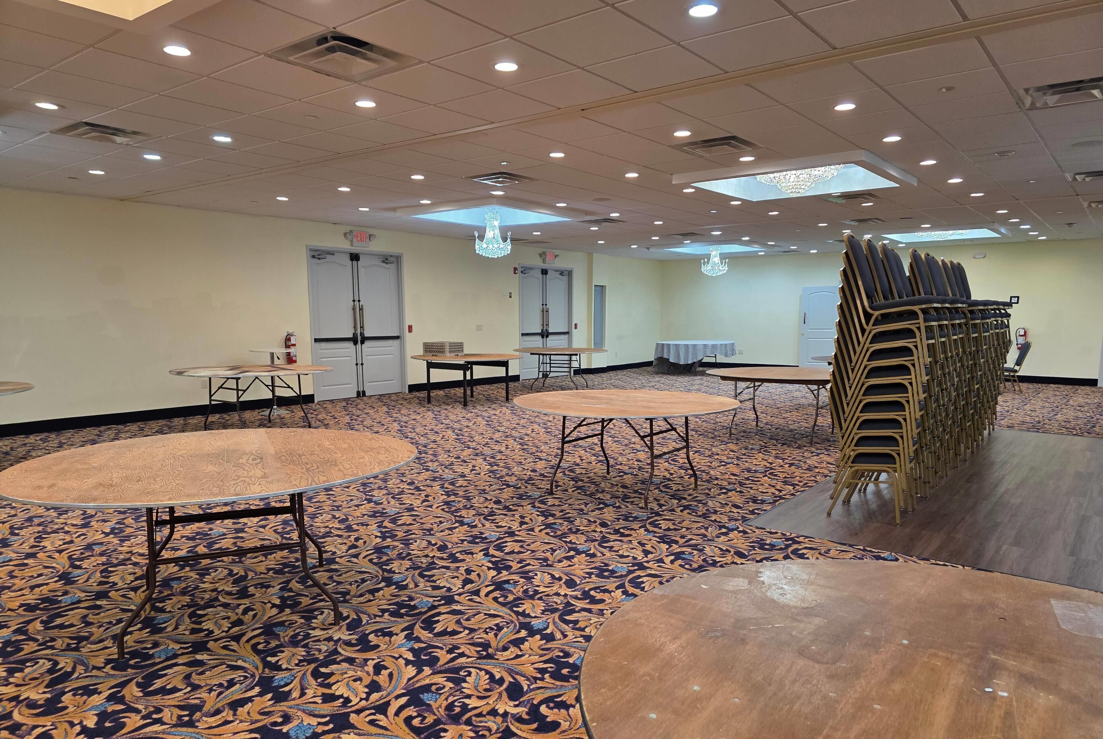A conference room with multiple tables and chairs, a patterned carpet, and a chandelier.