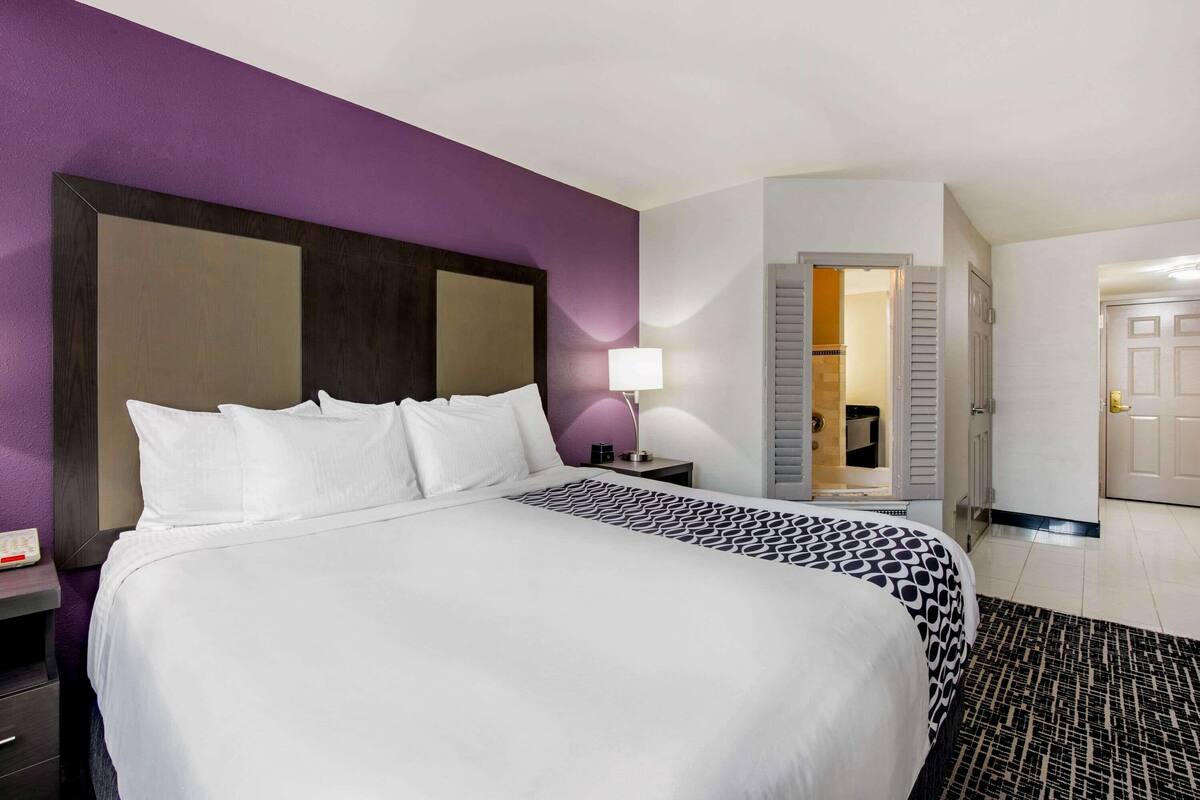 Une chambre d’hôtel avec un grand lit, une table de chevet, une lampe et une porte donnant sur une salle de bain.