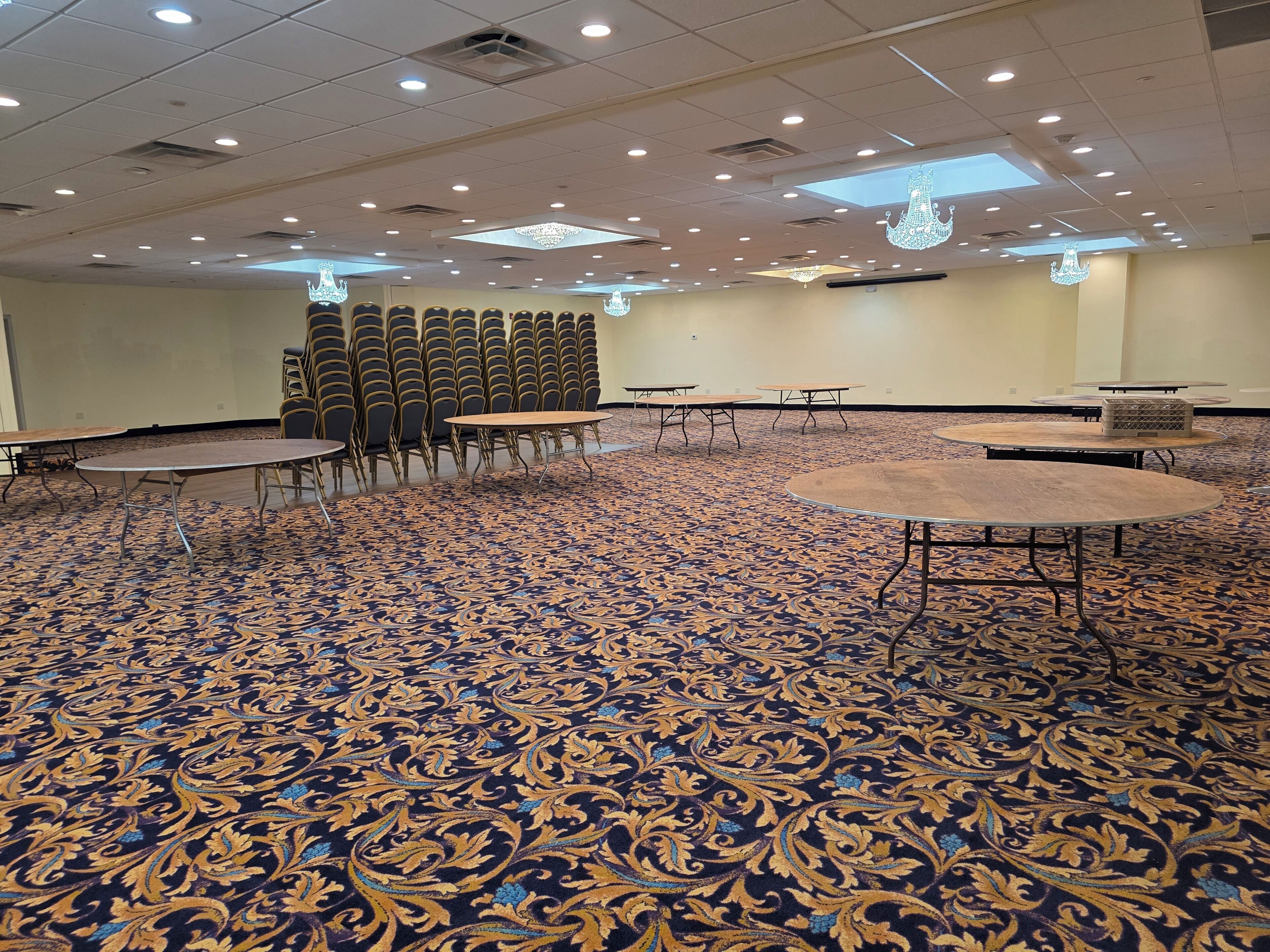 A conference room with patterned carpet, tables, chairs, and chandeliers.