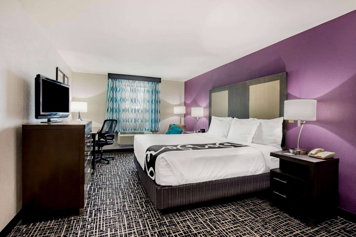 Une chambre d’hôtel avec un lit, un bureau, une télévision et une fenêtre avec des rideaux.