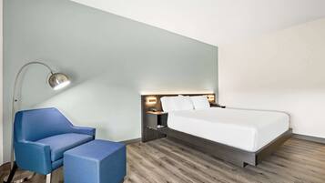A modern hotel room with a bed, a blue armchair, a side table, and a floor lamp.
