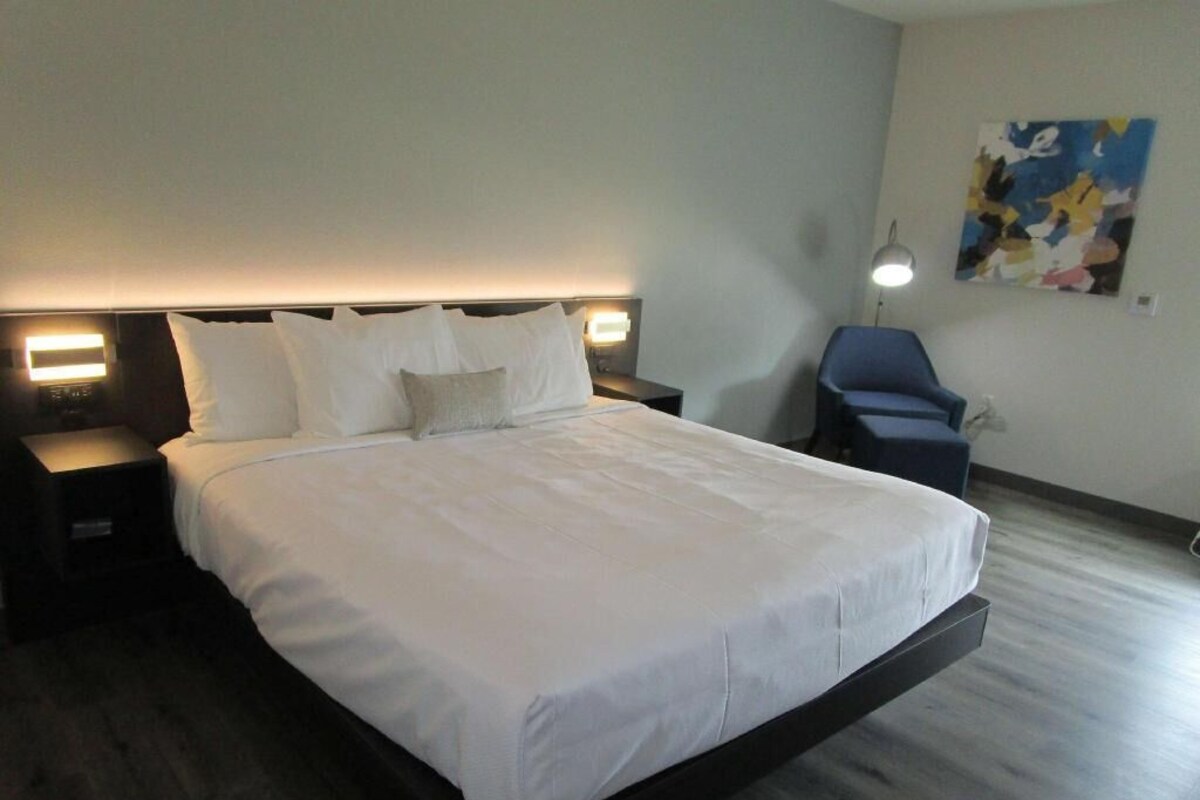 A hotel room with a large bed, bedside tables, a desk, a chair, and a painting on the wall.