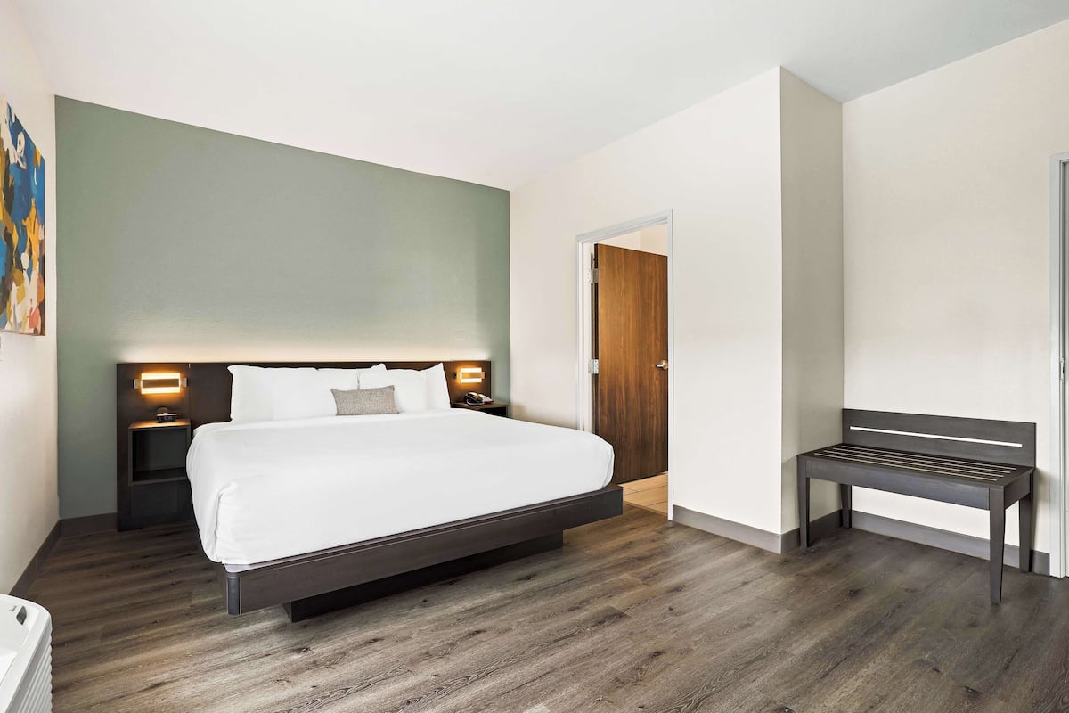 A modern hotel room with a large bed, bedside tables, a bench, and a door.