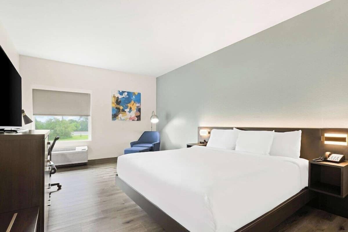 A hotel room with a large bed, a desk with a computer, a chair, a window with a view, and a painting on the wall.