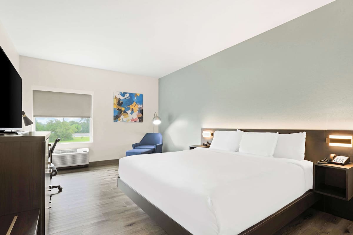 A hotel room with a large bed, a desk with a lamp, a chair, and a window with a view.