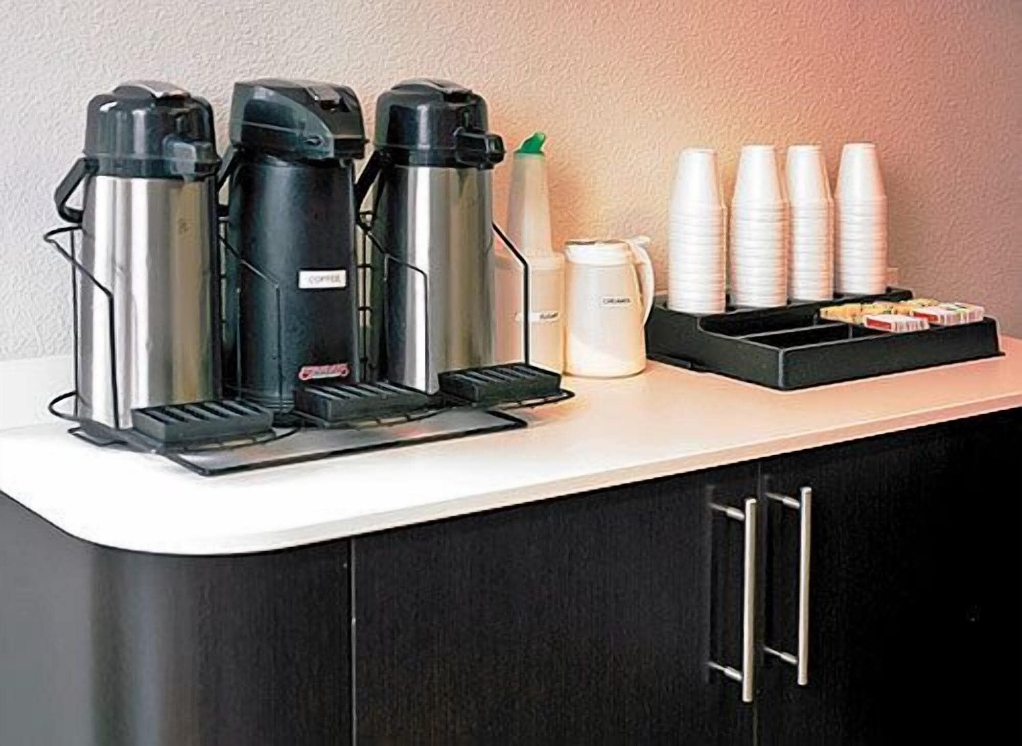 Una estación de café con tres máquinas de café, vasos desechables y una bandeja de pasteles.