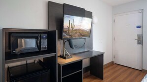Hotelkamer met een flatscreen televisie aan de muur, een magnetron en een klein bureau met een lamp.