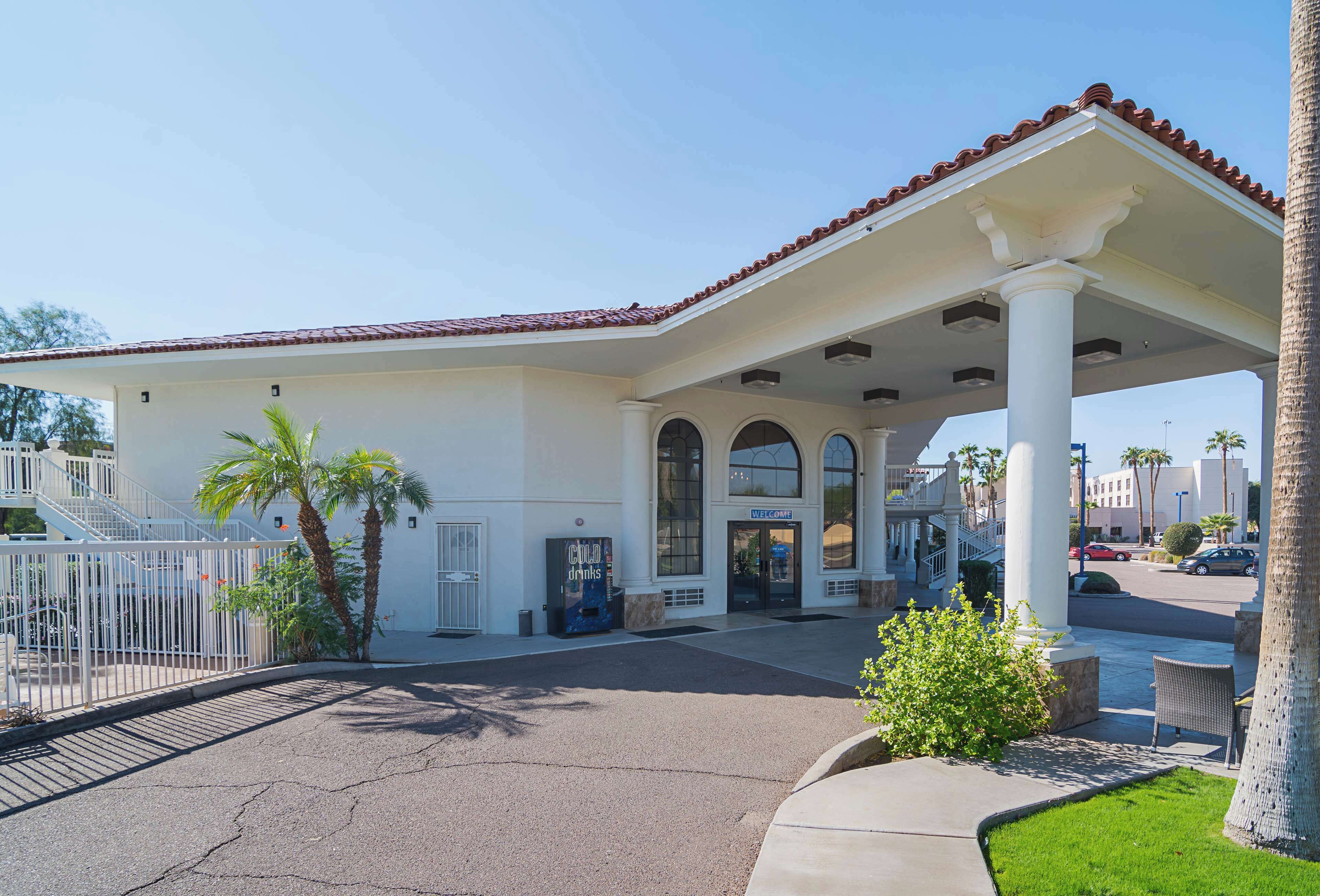 A hotel entrance with a covered patio, palm trees, and a clear sky.