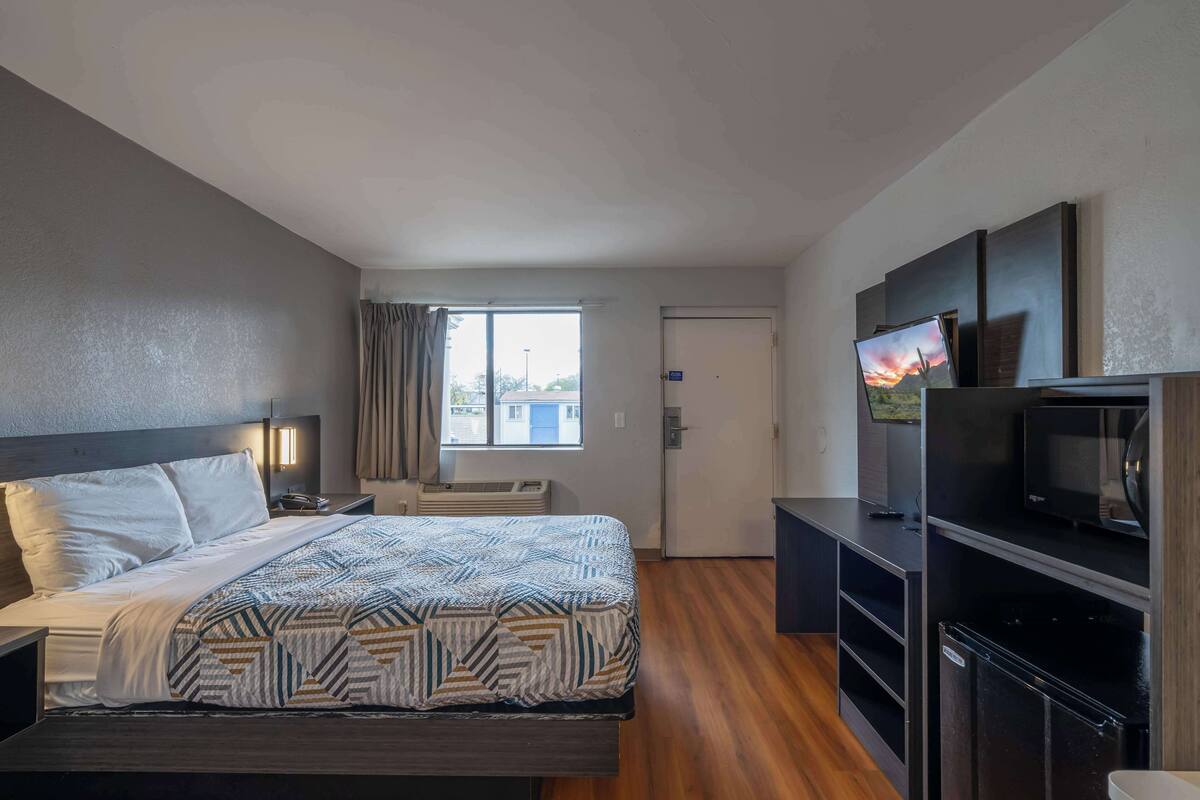 Una habitación de hotel con cama, escritorio, televisor y refrigerador.