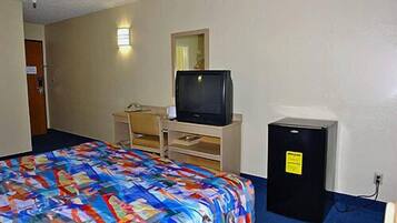 Una camera d'albergo con un letto, una scrivania con un computer, una televisione e un piccolo frigorifero.