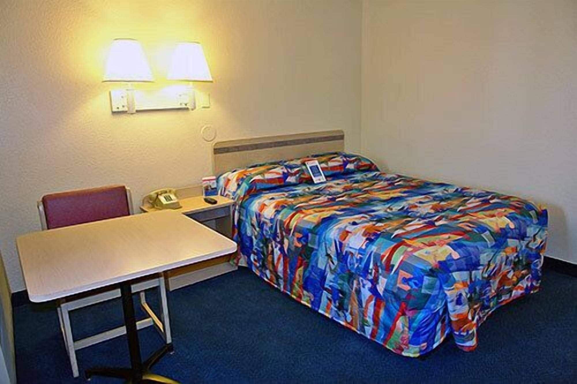 A hotel room with a bed, a desk, a chair, and a phone on the desk.
