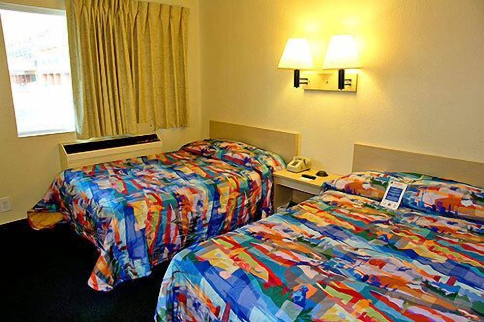 Une chambre d’hôtel avec deux lits, une table de chevet avec une lampe, un téléphone et une fenêtre avec des rideaux.